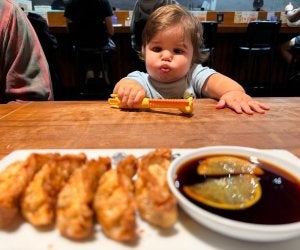 toddler sitting at restaurant table looking at dumplings